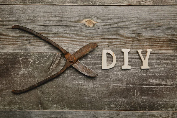 Top view of vintage rusty carpentry scissors and do it yourself sign on wooden background — стоковое фото