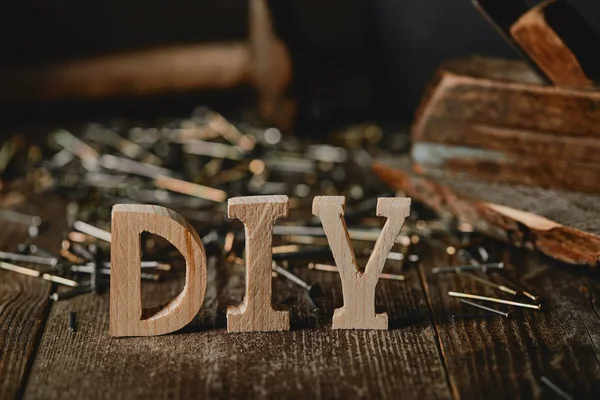 Feche o sinal de diy na mesa de madeira escura no fundo de pregos e logs — Fotografia de Stock