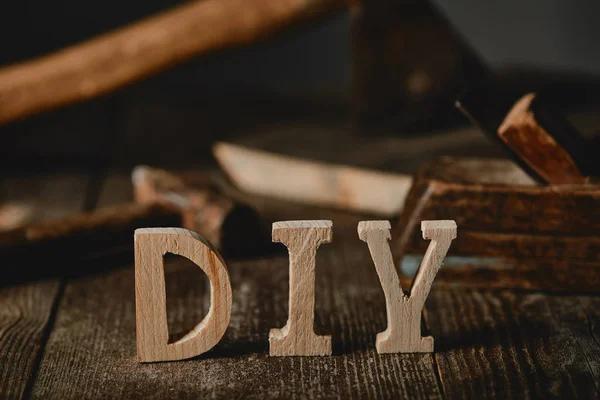 Nahaufnahme von diy Zeichen auf Holztisch auf dem Hintergrund von Werkzeugen und Baumstämmen — Stockfoto
