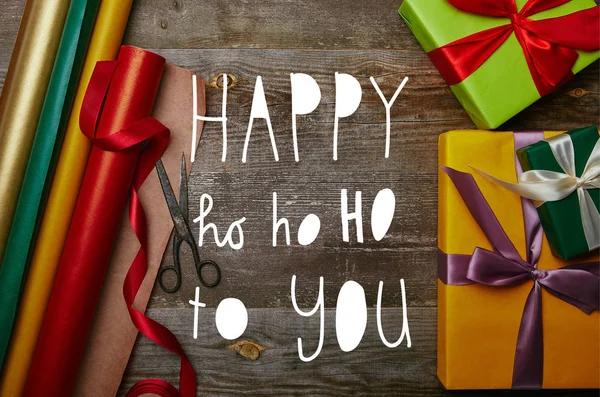 Top view of arrangement of wrapping papers, christmas presents with ribbons and scissors on wooden tabletop with 