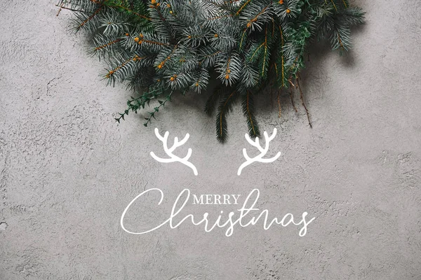 Обрезанный образ елового венка для украшения Рождества висит на серой стене с надписью 