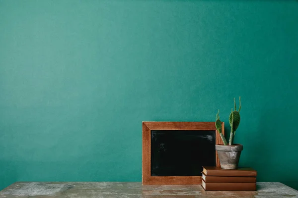 Cactus on books and wooden empty photo frame on green background — Stock Photo