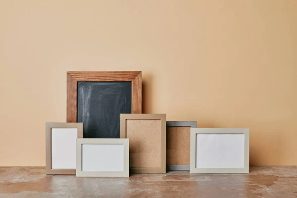 Different empty photo frames on dusty table on beige background — Stock Photo