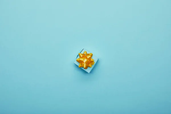 Top view of bright gift box with golden bow on blue background — Stock Photo