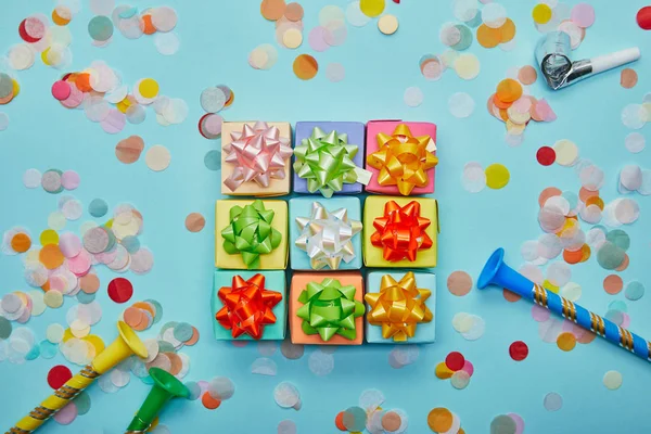 Top view of colorful gifts with bows, party horns and confetti on blue background — Stock Photo