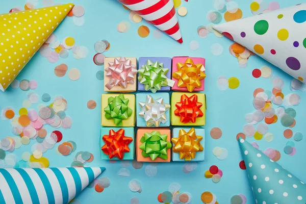 Vista superior de los regalos de colores con arcos, sombreros de fiesta y confeti sobre fondo azul - foto de stock