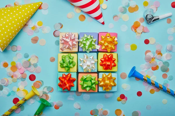 Draufsicht auf verschiedene bunte Geschenke mit Schleifen, Partyhüten und Konfetti auf blauem Hintergrund — Stockfoto