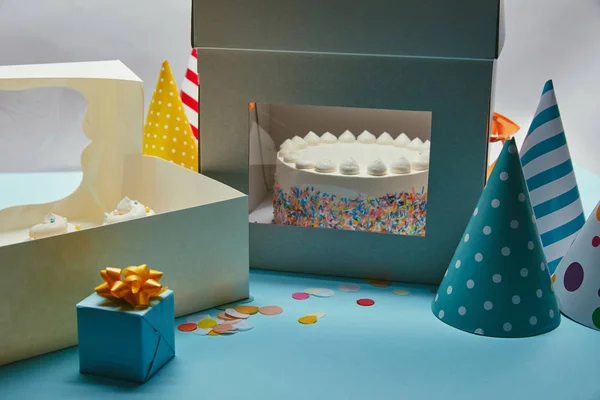 Delicious cake with meringues in box, cupcakes, gift and party hats on table — Stock Photo