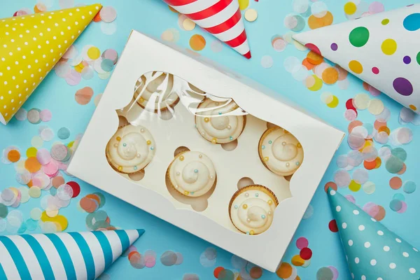 Blick von oben auf leckere Cupcakes, Partyhüte und Konfetti auf blauem Hintergrund — Stockfoto