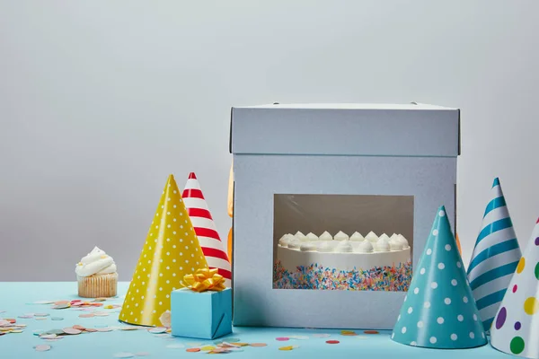 Bolo de aniversário, chapéus de festa, presente e cupcake na mesa no fundo cinza — Fotografia de Stock