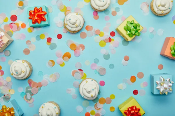 Draufsicht auf leckere Cupcakes, Konfetti und Geschenke auf blauem Hintergrund — Stockfoto
