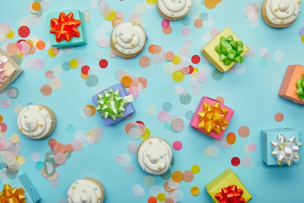Top view of delicious cupcakes, confetti and gifts on blue background — Stock Photo