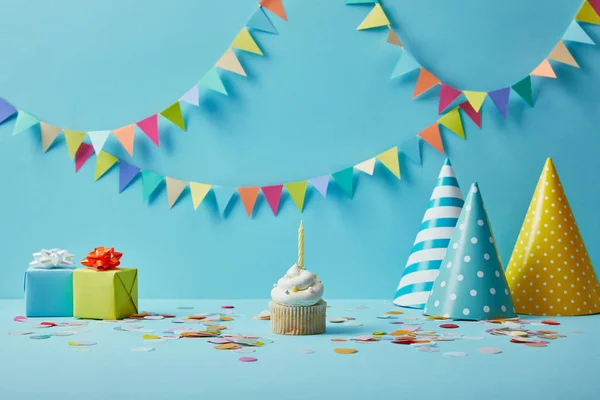 Délicieux cupcake, chapeaux de fête, confettis et cadeaux sur fond bleu avec bunting coloré — Photo de stock