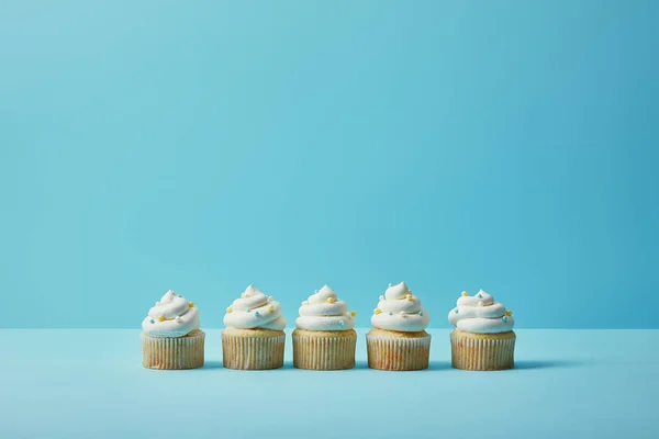 Deliciosos cupcakes com polvilhas de açúcar no fundo azul — Fotografia de Stock