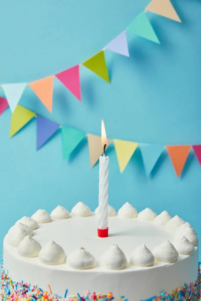 Candle on tasty birthday cake on blue background with bunting — Stock Photo