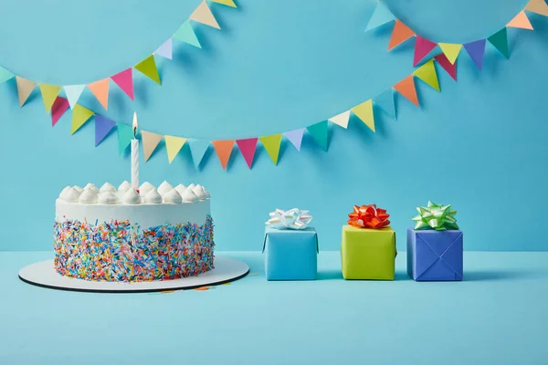 Gâteau savoureux avec des pépites de sucre et des cadeaux sur fond bleu avec un bruant coloré — Photo de stock