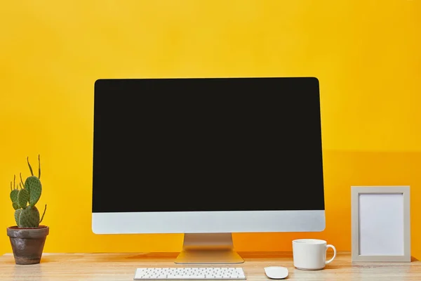 Computer, cactus in pentola e tazza di caffè al tavolo di legno su giallo — Foto stock