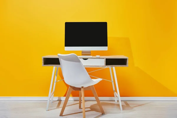 Ordenador con pantalla en blanco en mesa de madera con silla cerca de la pared amarilla - foto de stock