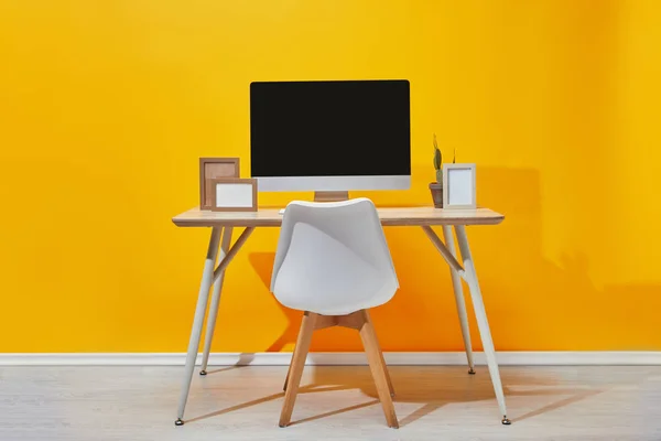 Computador, molduras para fotos e cacto no local de trabalho perto da parede amarela — Fotografia de Stock