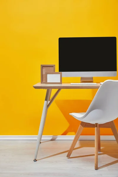 Computer and photo frames at wooden table near yellow wall — Stock Photo