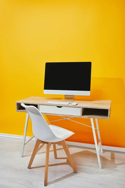 Computer with blank screen at wooden table and chair near yellow wall — Stock Photo