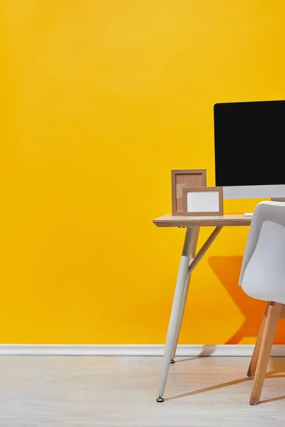 Ordenador y marcos de fotos vacíos en el lugar de trabajo cerca de la pared amarilla — Stock Photo