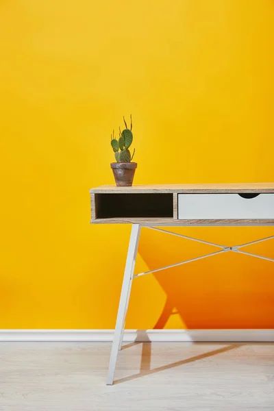 Kaktus im Blumentopf am Holztisch mit gelber Wand im Hintergrund — Stockfoto