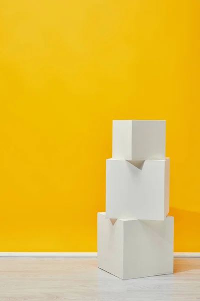 Minimalista cubos de yeso blanco dispuestos verticalmente cerca de la pared amarilla - foto de stock