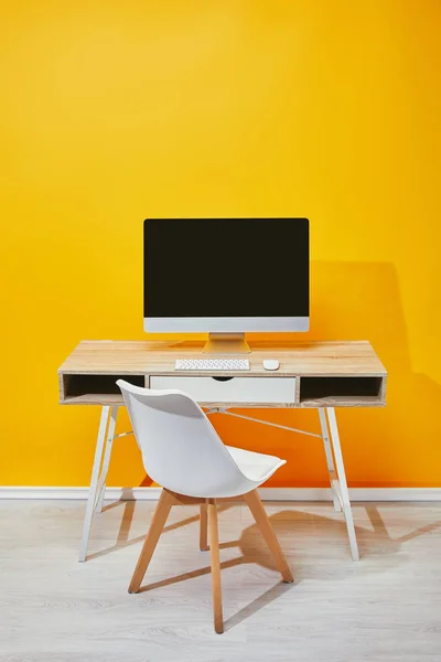 Компьютер на рабочем месте со стулом и желтой стеной на заднем плане — стоковое фото