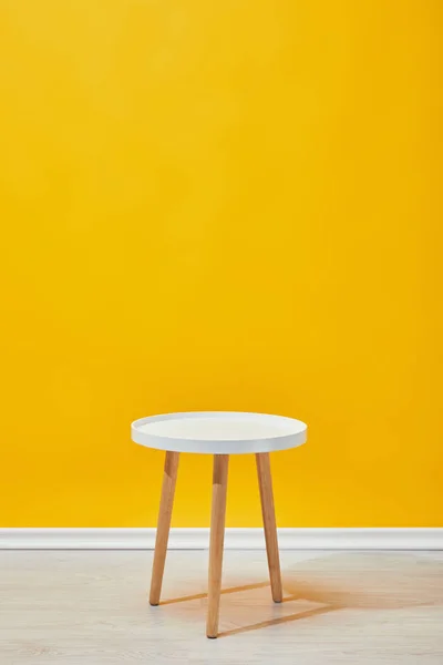 Минималистичный деревянный столик возле жёлтой стены — стоковое фото