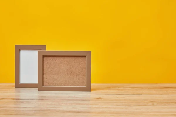 Empty photo frames at wooden table isolated on yellow — Stock Photo