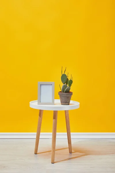 Cactus et cadre photo sur la table basse près du mur jaune — Photo de stock