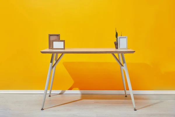 Wooden table with photo frames and cactus near yellow wall — Stock Photo