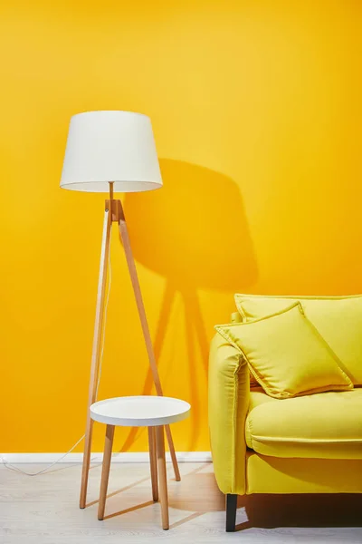 Sofá com travesseiros, lâmpada de assoalho e mesa de café perto da parede amarela — Fotografia de Stock