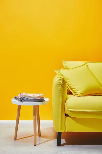 Sofá con almohadas y mesita con revistas cerca de la pared amarilla — Stock Photo