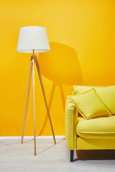 Sofá com travesseiros e lâmpada de assoalho com parede amarela no fundo — Fotografia de Stock
