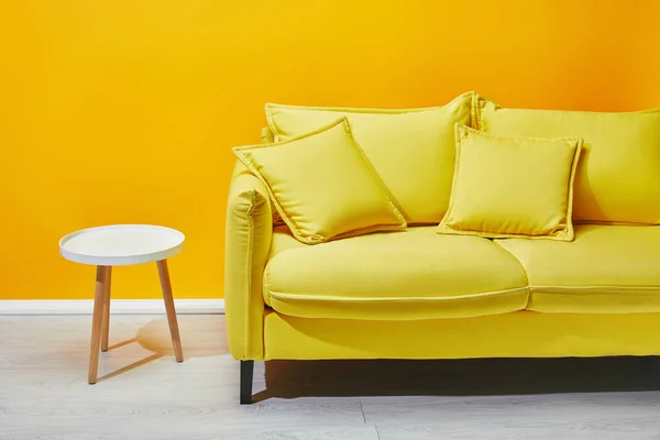 Желтый диван и белый журнальный столик возле яркой стены — стоковое фото