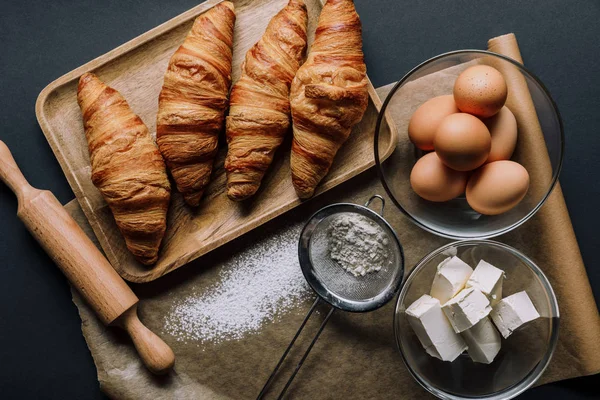 Elevated view of baking paper covered by flour, croissants and ingredients on table — Stock Photo