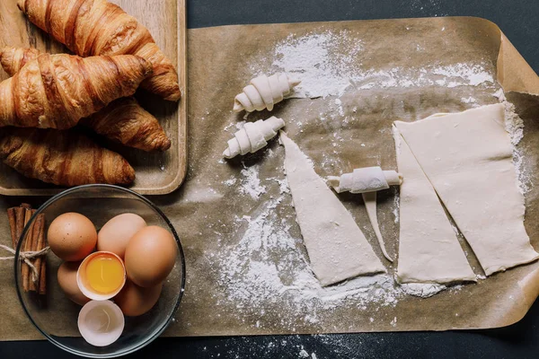 Vue du dessus du papier cuisson avec pâte pour croissants, oeufs et cannelle à la surface — Photo de stock