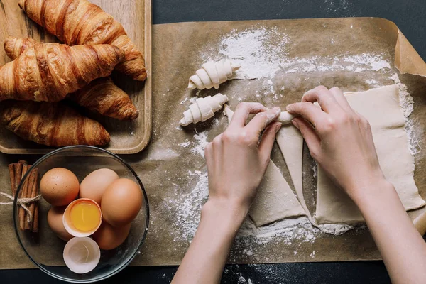 Обрізане зображення жінки, що прокатує тісто для круасанів на папері для випічки, покритому борошном поблизу інгредієнтів — стокове фото