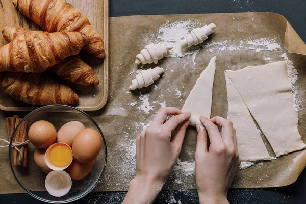 Vista parziale della donna rotolamento pasta per croissant su carta da forno coperto da farina vicino ingredienti — Foto stock