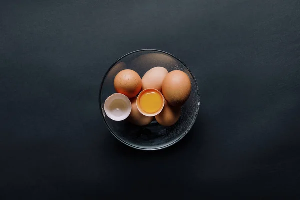 La vista de arriba de los huevos de gallina en la escudilla a la mesa negra - foto de stock