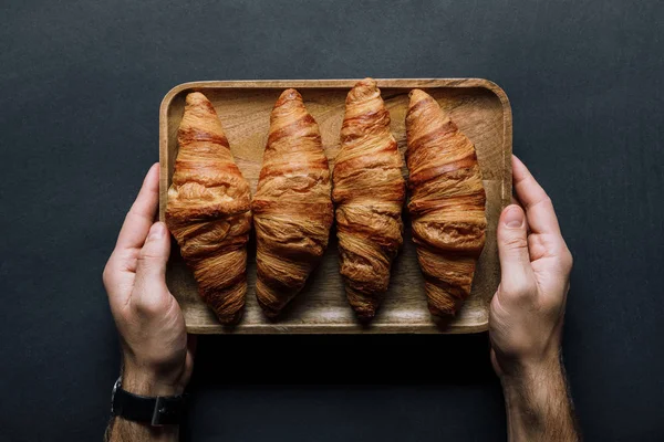 Cropped image of man holding tray with croissants over black table — Stock Photo