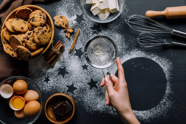 Visão parcial da mulher peneirando farinha através da peneira sobre a mesa coberta de farinha com símbolos de estrelas e biscoitos com ingredientes — Fotografia de Stock