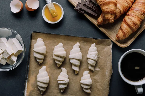 Vue surélevée du plateau avec pâte pour croissants, ingrédients et tasse à café sur table noire — Photo de stock