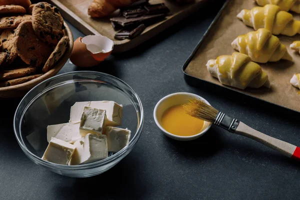 Selektiver Fokus von Butter und Eigelb mit Pinsel nahe Tablett mit Teig für Croissants auf dem Tisch — Stockfoto