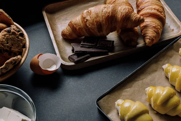 Close up view of dough for croissants on tray with baking paper surrounded by ingredients on black table — Stock Photo
