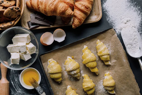 Leigos planos com massa para croissants na bandeja, gema de ovo com escova e ingredientes na mesa coberta de farinha — Fotografia de Stock