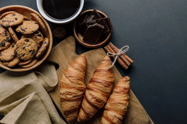 Elevated view of coffee, croissants, chocolate and cookies on black table — Stock Photo