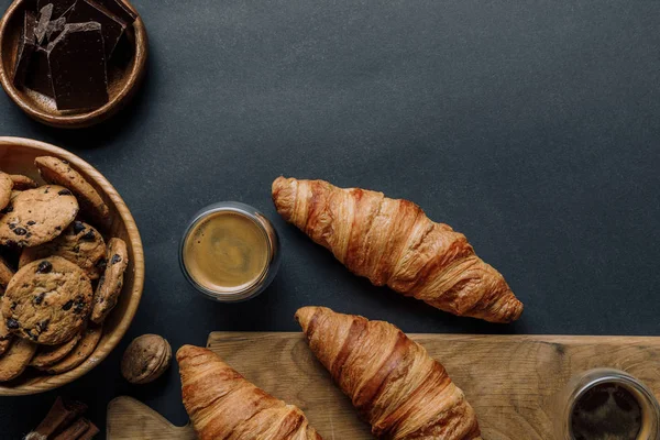 Flache Liege mit Walnuss, Kaffee, Croissants, Schokolade und Keksen auf schwarzem Tisch — Stockfoto